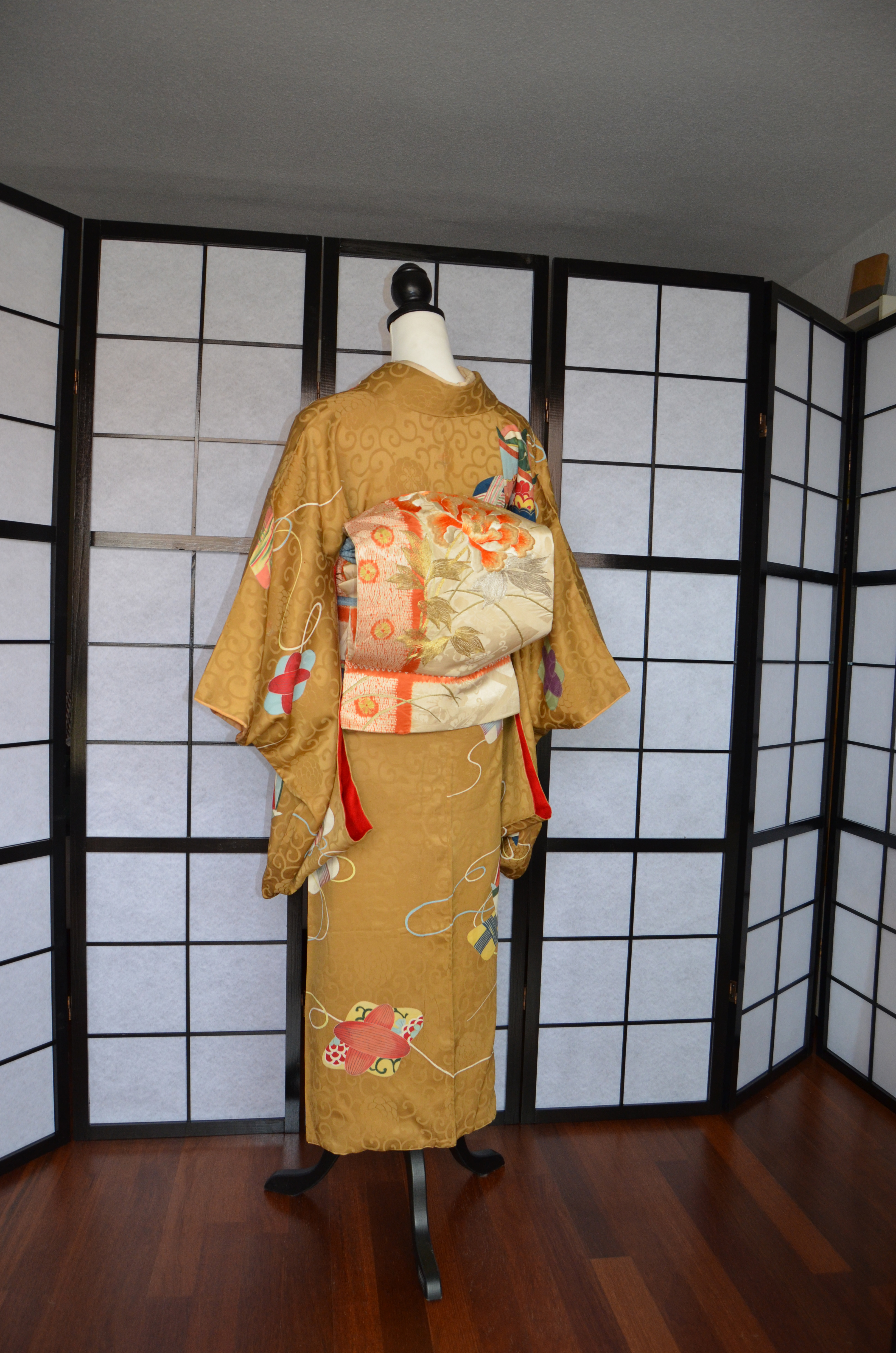 Kimono amarillo visto por su parte trasera, frente a un biombo a cuadros.