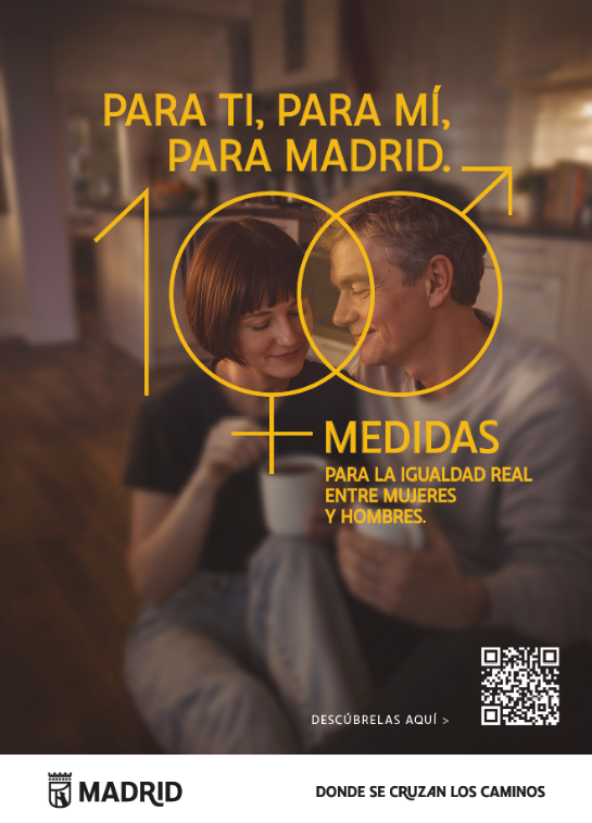Cartel vertical con una fotografía en primer plano de dos personas adultas interactuando en un espacio interior cálido. Se aprecia una situación de conversación cercana, cotidiana, que transmite conexión y complicidad. A la izquierda, sobre un fondo oscuro, aparece el mensaje en letras amarillas: “Para ti, para mí, para Madrid. Medidas para la igualdad real entre mujeres y hombres. Descúbrelas aquí